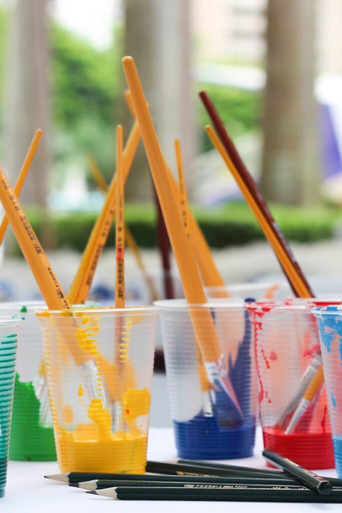 Vibrant paint brushes and pencils in plastic cups for arts and crafts.